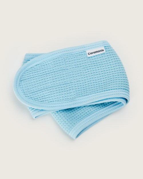A soft, blue, textured cloth with a label 'Ceremonia' on it, folded neatly on a white background.