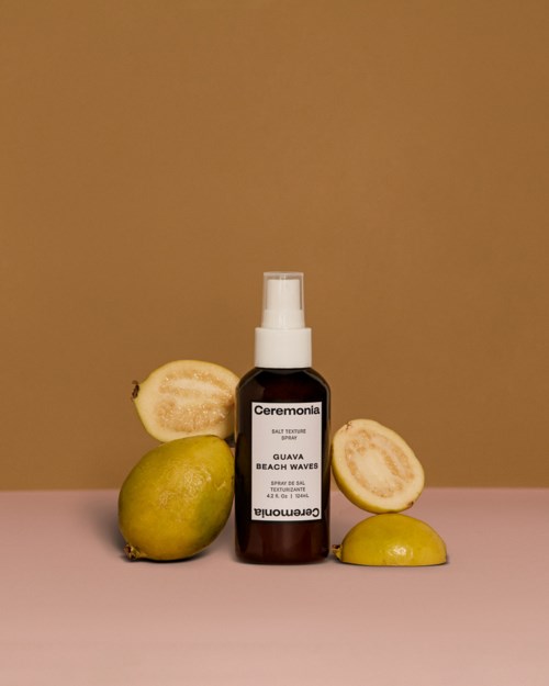 En sprayflaska märkt 'Guava Beach Waves' omgiven av guavabitar och hela guavon.