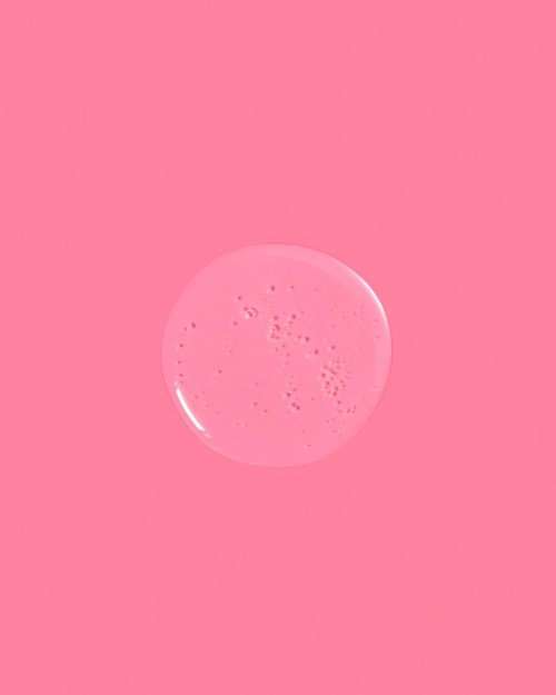 En rund, klar rosa tvålbubbla vilar på en rosa bakgrund.