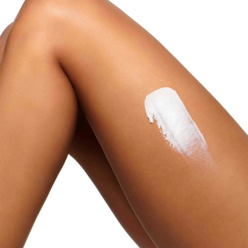 En kvinna applicerar vit lotion eller kräm på låret. Hudytan är slät och solbränd.