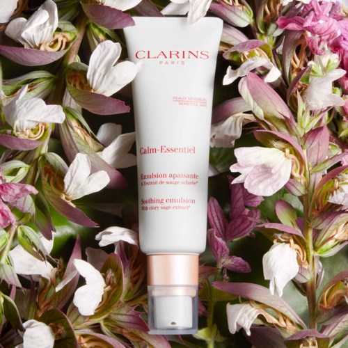 Eine weiße Tube mit Clarins Paris, umgeben von pinken und weißen Blumen mit grünen Blättern.