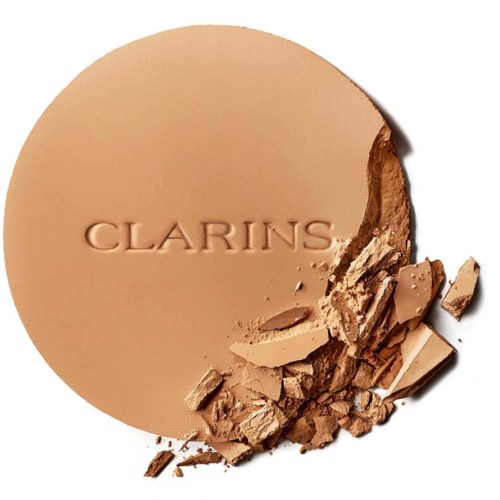 A round makeup powder compact with the Clarins logo, some powder is broken and scattered around.