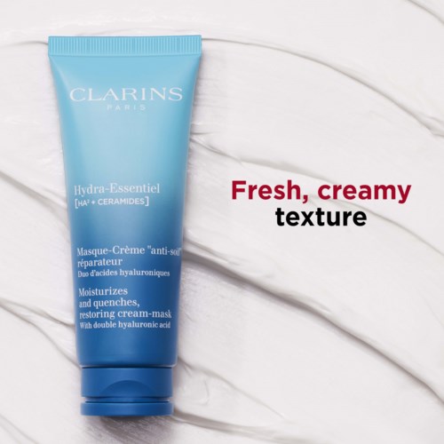 En blå tub med Clarins ansiktskräm, med vit och röd text, ligger på en vit texturerad yta.
