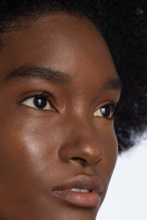 Een close-up van een vrouw met een gladde huid, natuurlijke make-up en grote, expressieve ogen die wegkijken.