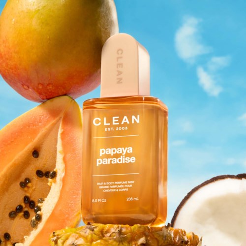 Hellorange Haar- und Körperspray mit Papayageschmack, umgeben von frischer Papaya und Kokosnötter gegen blauen Himmel.