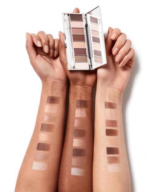 En person håller i en ögonskuggspalett med bruna och beige nyanser, visar swatches på armarna.