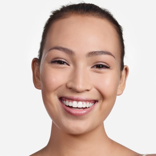En kvinde med et bredt smil, klar hud og håret trukket tilbage, ser glad og selvsikker ud.