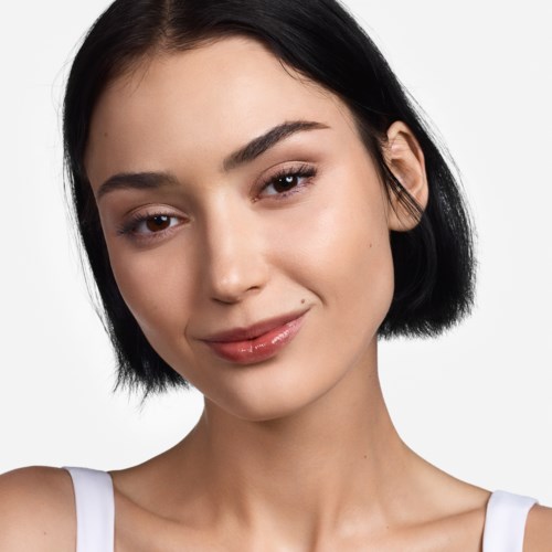 En ung kvinde med kort sort hår smiler blidt med neutral makeup.