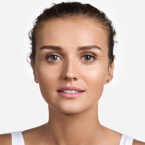 Młoda kobieta z czystą skórą, delikatnym makijażem i włosami odgrodzonymi do tyłu, patrzy prosto na kamerę z łagodnym uśmiechem.