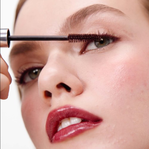 En kvinde påfører mascara på sit øje. Hun har lys hud og blondt hår. Fokus er på øjet og makeuppen.