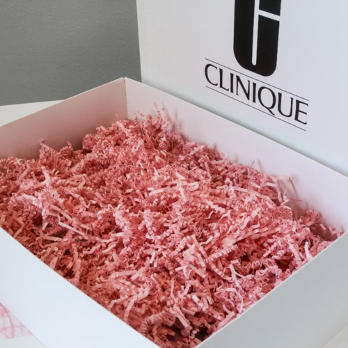 En hvid boks med pink strøet papir og en Clinique-shop bag bag.
