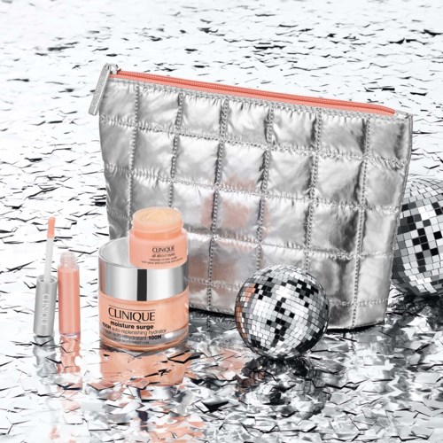 A shiny silver makeup bag with a peach-colored skincare jar, mascara, and disco balls on a reflective silver surface.