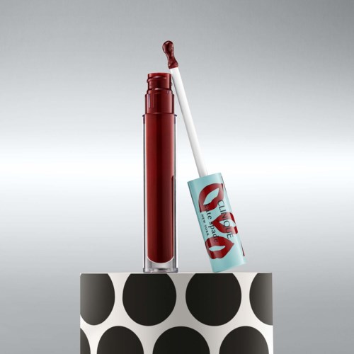 Roter Lippenstift mit Applikator, leicht geöffnet, auf einer weißen und schwarzen Polka-Dot-Plattform.