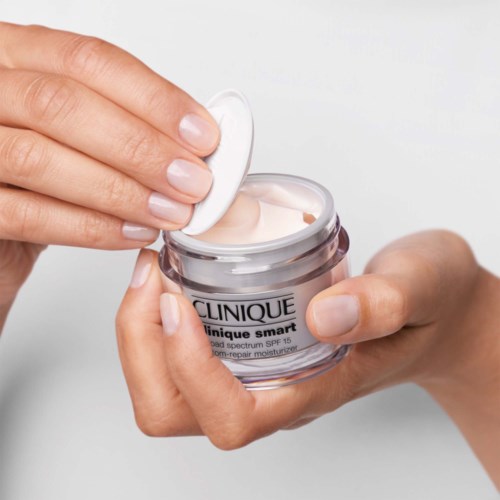 En person åbner et glas med Clinique fugtighedscreme, der viser en lys creme indeni.