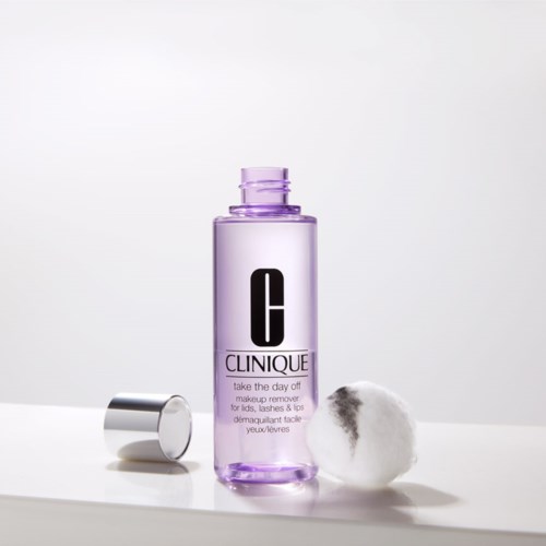 Een Clinique make-up remover fles met een wattenschijfje ernaast op een witte ondergrond.