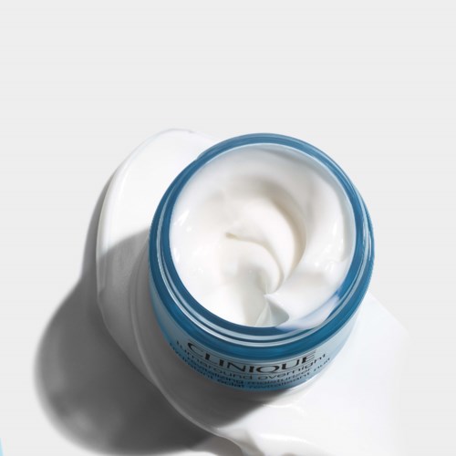 A jar of white cream with a blue lid, partially open, on a white surface. The cream looks smooth and thick.