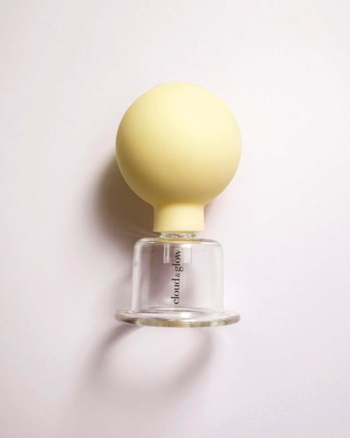 A glass perfume bottle with a round, yellow cap on a white background.