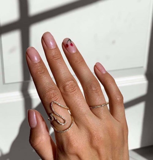 Een hand met ringen, nagelkunst en een kleine kers-tatoeage op de middelvinger.