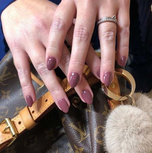 Händer med välskötta naglar och ringar, vilande på en designerväska med en pälsnyckelring.