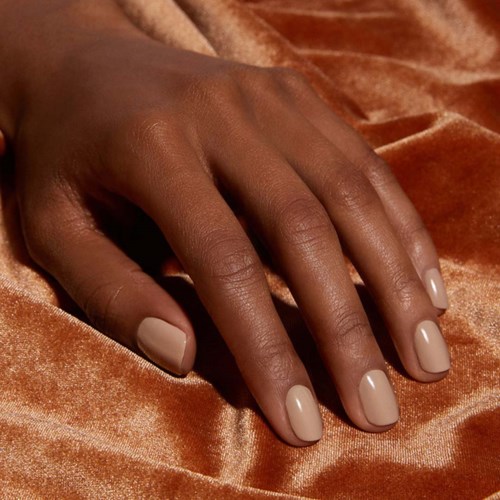 Een hand met netjes gelakte beige nagels rust op glanzende, oranje-bruin doek.