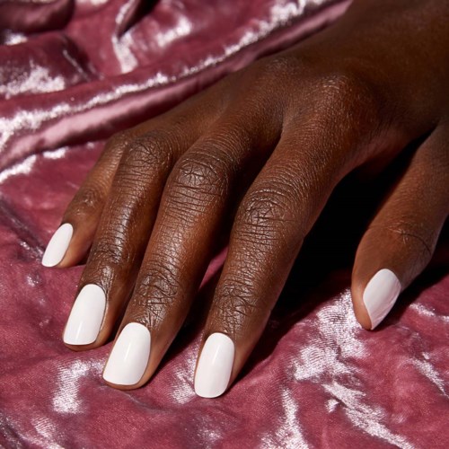 Een hand met een donkere huid en witte nagels ligt op roze, glanzende stof.