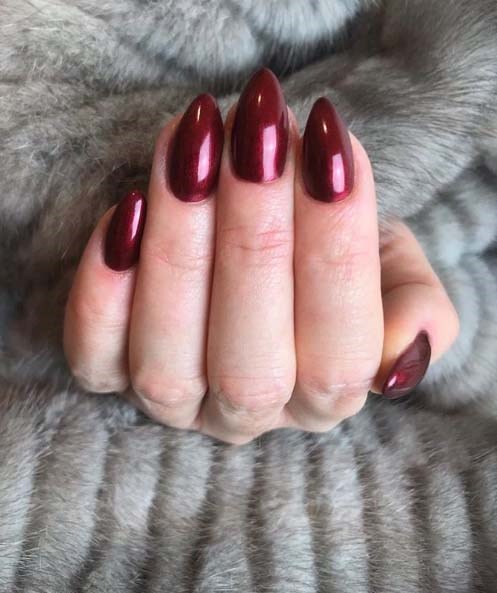 Een hand met glanzende donkerrode nagels rust op een grijs harig oppervlak.