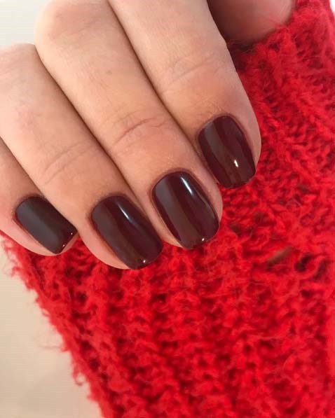 Hand met donkerrode of wijnrode gelakte nagels rust op een rood, textured stof.