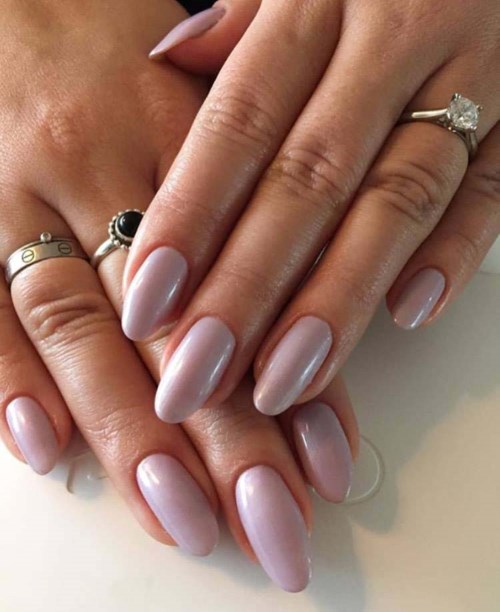 Twee handen met goed verzorgde nagels en verschillende ringen, waaronder een grote steenring. De nagels zijn lichtroze.