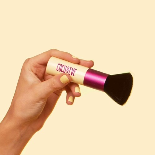 Eine Hand hält einen Make-up-Pinsel mit pinkem und schwarzem Griff, und der Schriftzug 'COCO & EVE' auf dem Griff.