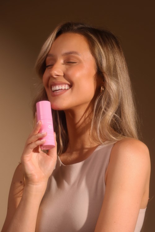 En kvinna applicerar glädjesamt rosa läppbalsam, ler med stängda ögon och visar frisk hud.