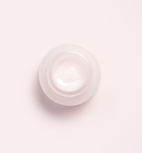 En liten rund vit behållare med ett genomskinligt lock, kanske för lagring av kräm eller lotion.