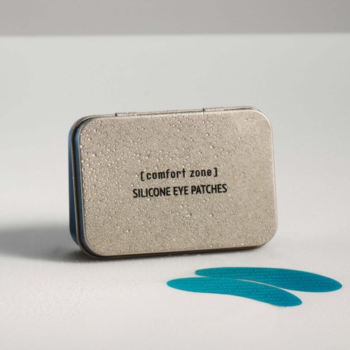 A small gray tin box labeled comfort zone silicone eye patches, with two blue patches placed in front.
