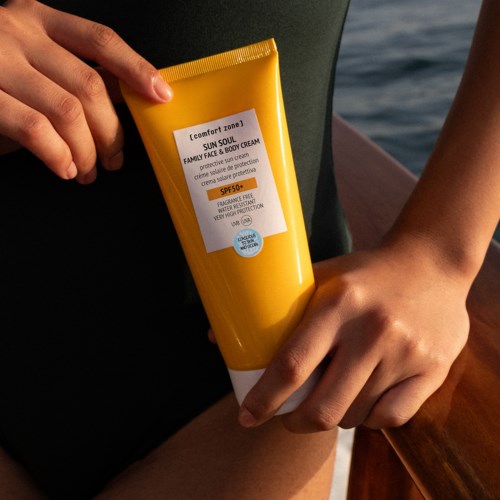 Person håller i ett gul-rör med solskyddscreme nära vattnet. Krämen har SPF 50.