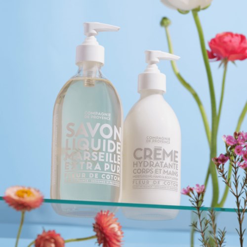 Two white bottles with pump dispensers are placed among colorful flowers against a light blue background.