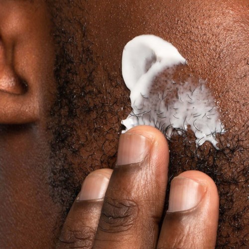 Finger, der trägt weiße Creme auf dunkler Haut nahe Haar auf. Nahaufnahme eines Hautpflege- oder Kosmetikprozesses.