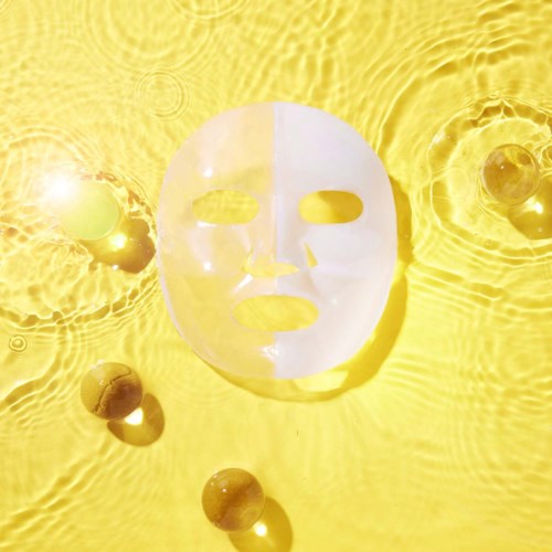 En hvit ansiktsmaske flyter på gult vann, med noen små runde gjenstander i nærheten, som reflekterer sollys.