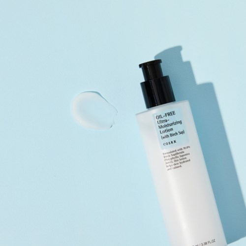 En hvit flaske med fuktighetskrem og svart pumpe på en lyseblå bakgrunn, med litt lotion som er sølt ved siden av.