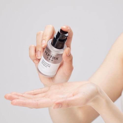En hand håller en liten flaska märkt 'PEPTIDE 132', antyder hudvård eller kosmetik.