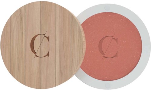 En liten rund makeuppakning med ett trälock och rosa puder inuti, med bokstaven 'C' ingraverad.