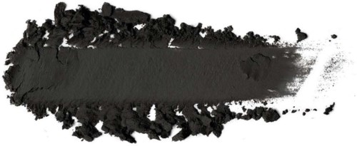 Black powder spread on a white surface. It is uneven with some clumps and a brush stroke pattern.