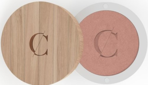 A wooden round cover and a pink makeup compact with a 'C' logo. The cover is open, showing the compact inside.
