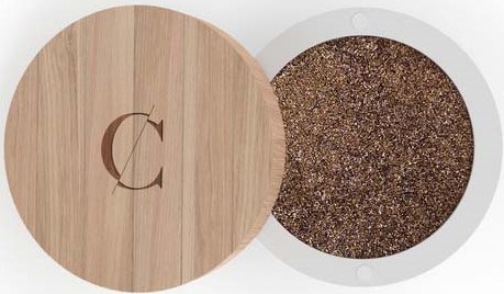 A round wooden container with a letter 'C' on the lid and a sparkly brown makeup product inside.