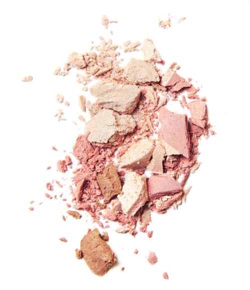 Zerbrochenes Rouge-Puder in Pink- und Beigetönen, verstreut auf weißem Hintergrund.