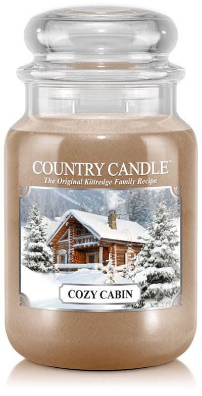 En stor lysestake merket 'Cozy Cabin' med bilde av en snødekt hytte og trær.