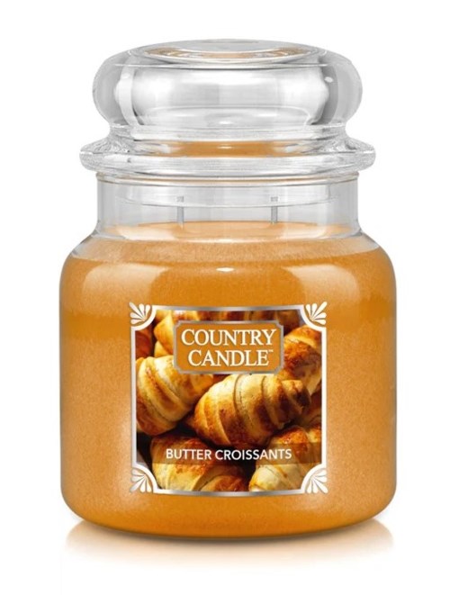Ett ljus i burk med etikett som visar smörcroissanter och ett klart glaslock.