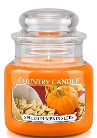 Ett ljus i glas med orange vax och etikett med pumpafrön och pumpa.