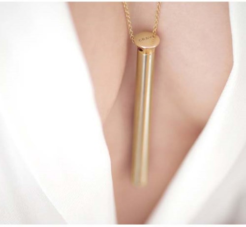 A gold chain with a long, cylindrical pendant worn around the neck. The pendant is shiny and smooth.