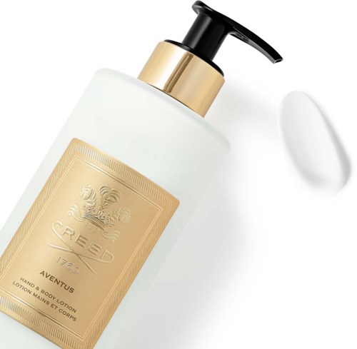 En vit flaska med guldbelagt etikett och svart pump, bredvid en liten mängd vit lotion eller kräm.
