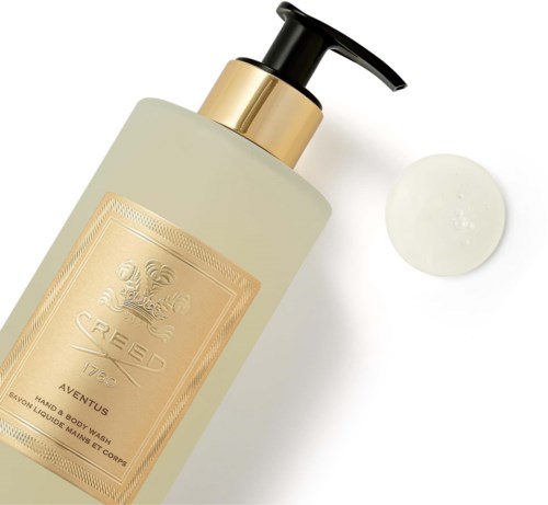 En flaska med lotion eller flytande tvål med svart pump, guldig etikett och lite kräm bredvid.