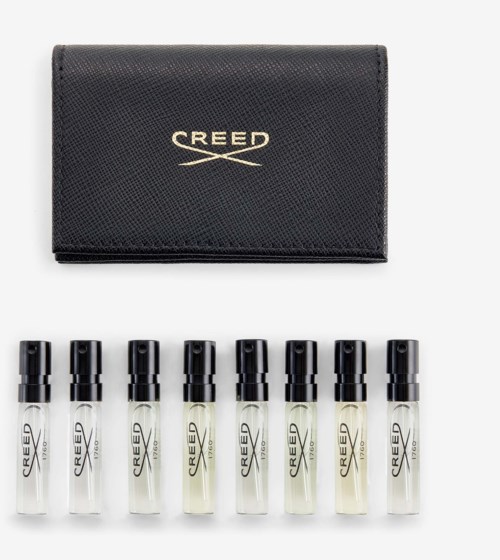 Yhdeksä pieniä läpinäkyviä pulloja mustilla korkeilla ja CREED-pakkaus niiden takana.